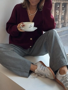 Detailed shot of burgundy v-neck cardigan with gold buttons and grey wide-leg trousers