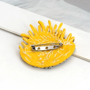 Close-up of yellow embroidered brooch back with metal safety pin and felt base