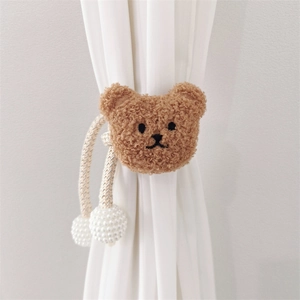 Detail of plush brown bear curtain tieback with cream woven rope on white sheer fabric