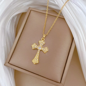 Golden cross necklace with white rhinestones on beige jewelry box and white silk