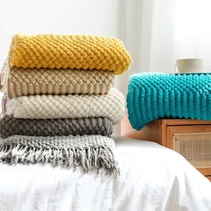 Close-up of textured knit blankets with pom-pom patterns and fringe in multiple colors