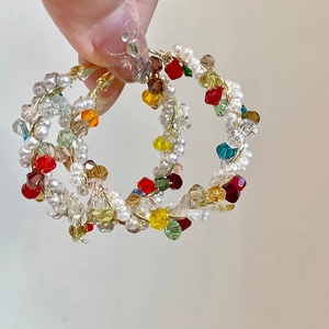 Détail de créoles faites main avec des perles de cristal colorées et des perles blanches dorées