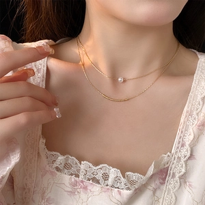 Close-up of a double-layered gold necklace with baroque pearl worn on model's neck