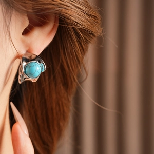 Close-up of vintage silver C-shaped earring with turquoise stone worn by a model