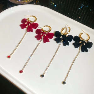 Detail of red and black velvet bow earrings with long rhinestone tassels on a tray