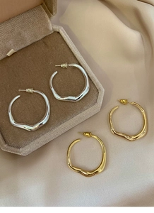Detail showing irregular wavy hoop earrings in gold and silver finish on velvet