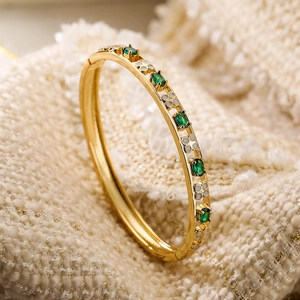 Brazalete bañado en oro 18K con piedras verdes y trébol de esmalte sobre fondo tejido