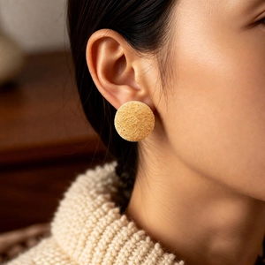 Close-up of golden matte textured round stud earrings on a model wearing a sweater
