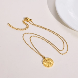 Detail of gold stainless steel necklace featuring a sunburst pendant and lobster clasp