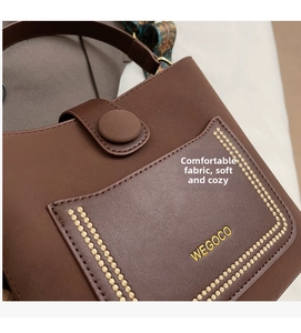 Detail of brown leather bucket bag with wide ethnic strap and gold logo engraving