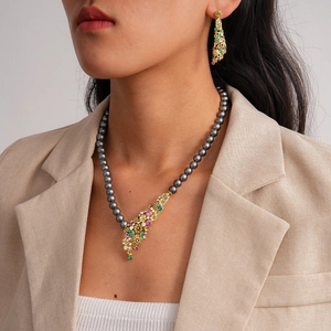 Detail of dark pearl necklace and flower pendant set on a model in a beige suit