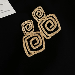 Close-up of golden square spiral textured earrings on a premium black fabric background