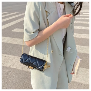 Close-up of black quilted cylinder bag with gold chain strap worn on woman's shoulder