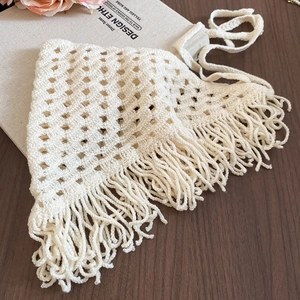 Detailed knit texture of cream crochet triangle scarf with long fringe on wood