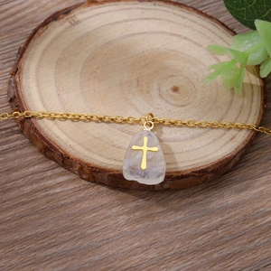 Minimalist gold chain necklace with white natural stone cross pendant on wood base