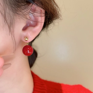 Detail of elegant gold studs with large red round drop earrings worn by a model