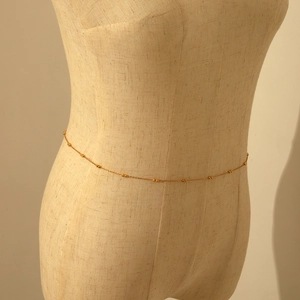 Detail view of a gold beaded layered waist chain displayed on a linen mannequin