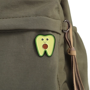 Detailed close-up of a cute avocado tooth enamel pin on a green canvas backpack fabric
