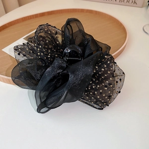 Détail d'une grande pince à cheveux à nœud en organza noir avec des pois dorés chics