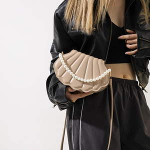 Detail view of a shell-shaped crossbody bag in beige with pearl chain and fan texture