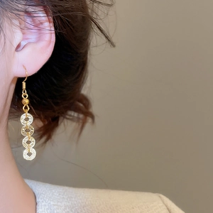 Close-up of elegant gold drop earrings featuring a triple ancient coin design on a model