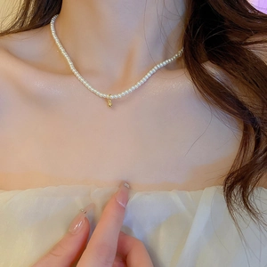 Gros plan d'un collier de perles blanches fines avec un pendentif boule dorée sur un modèle