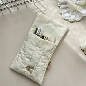 Close-up of quilted cream pouch featuring gold rabbit embroidery and snap button