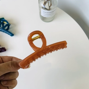 Détail d'une pince à cheveux en acrylique ambré tenue à la main sur un fond décoratif