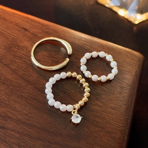 3-piece gold plated ring set with pearls and zircon charms on dark wood background