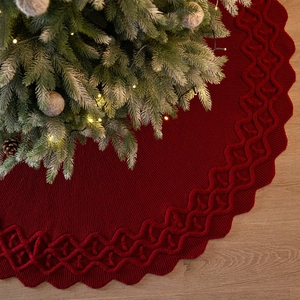 Red knitted Christmas tree skirt with decorative wavy edge on light wood floor background