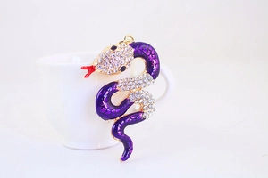 Detailed view of a purple enamel snake charm with white rhinestones on a gold ring hook