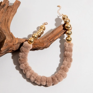 Détail du collier avec perles en métal doré, boules en peluche marron et fermoir mousqueton