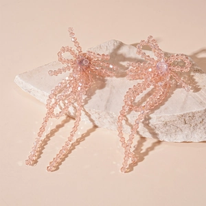 Pink crystal bow earrings with long beaded tassels on white stone decorative background
