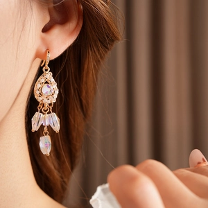 Close-up of golden vintage drop earrings with iridescent crystals worn by a model