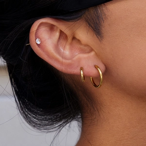 Gros plan de créoles dorées et d'un petit clou en diamant sur l'oreille du mannequin