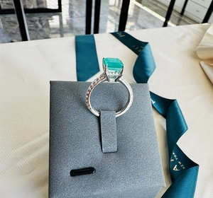 Close-up of emerald cut green gemstone ring with side-set diamonds on silver band