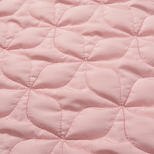 Close-up of pink quilted fabric featuring an elegant floral stitching pattern detail