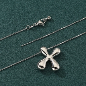 Minimalist silver X-shaped letter pendant necklace with fine box chain on green background