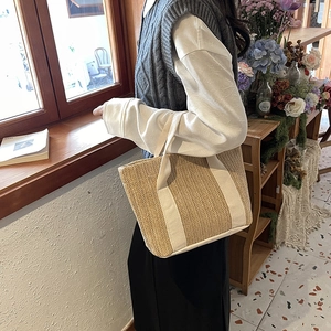 Detail view of woven straw tote bag with white canvas straps in a casual lifestyle setting