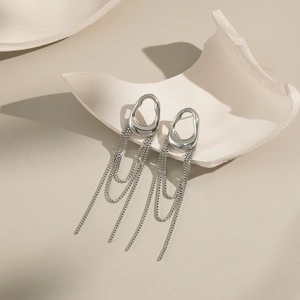 Close-up of silver geometric tassel earrings with box chain fringe on ceramic