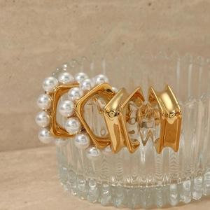 Minimalist C-shaped gold-plated earrings set with pearls on textured glass display