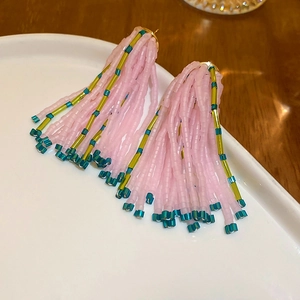 Detail view of pink beaded fringe earrings on a white ceramic plate and wooden background