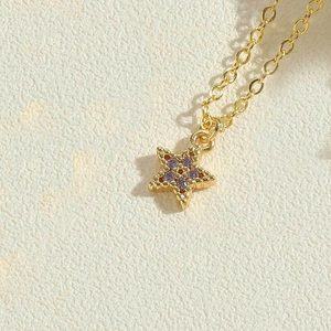 Macro detail of a golden star pendant necklace with delicate purple zircon inlay decor