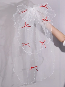 Detail of white bridal veil with red ribbon bows and hanging white pearl beads