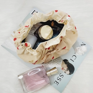 Beige corduroy makeup bag with red cherry patterns and a bow on white plush background