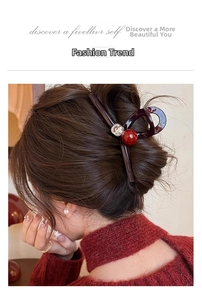 Détail macro d'une pince à cheveux en acrylique foncé avec perle rouge et strass brillant