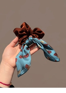 Close-up of elegant dark brown silk scrunchie with light blue printed bow ribbon detail