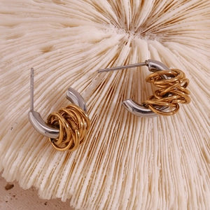 Macro view of C-shaped mixed metal earrings with gold rings on white coral texture