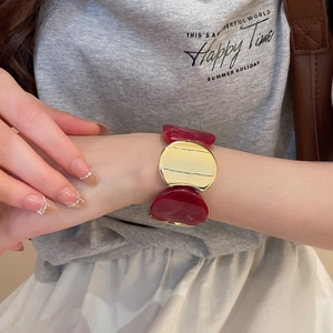 Bracelet élastique en acrylique et métal doré porté au poignet par un mannequin