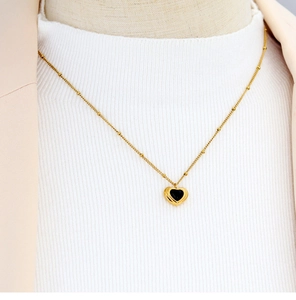 Detail of heart necklace with black agate stone inlay on a gold-plated beaded chain